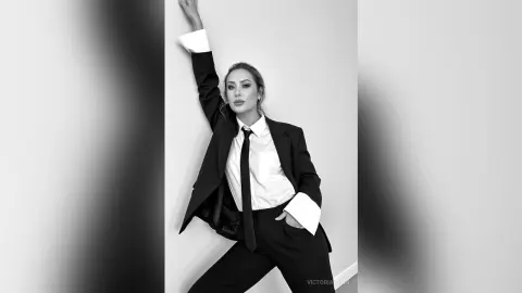 Elegant woman in a black suit and white shirt posing confidently in a minimalist studio setting.