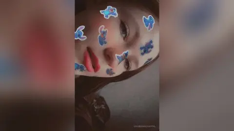 Close-up portrait of a young woman with playful blue cartoon stickers on her face in a soft, dreamy mood.