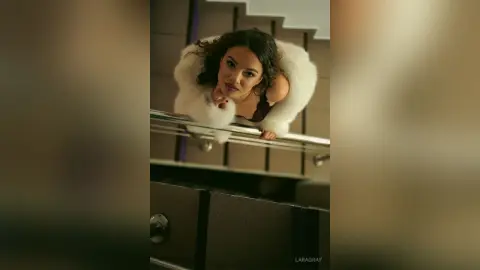 Elegant woman in a white faux fur coat posing on a modern staircase with a moody, cinematic atmosphere.