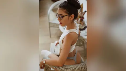 JessieLiu poses in a white tank top and grey thong, looking over her shoulder while sitting on a patterned chair.