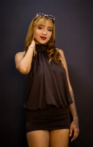 Elegant woman in a black halter top and mini skirt posing against a dark background.