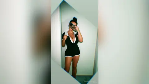 Stylish woman in a black romper with white trim posing for a mirror selfie in a bright room.