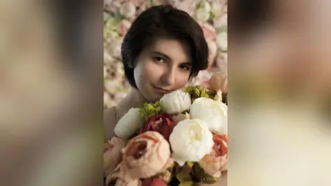 Young woman with short dark hair holding a large bouquet of white and pink peonies in a romantic floral setting.