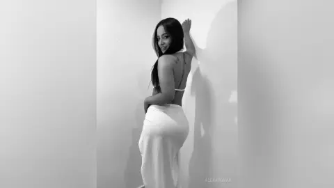 Elegant woman in a white backless dress posing against a minimalist white wall in a moody black and white portrait.