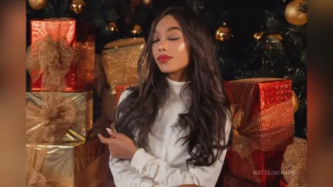 Beautiful woman in a white turtleneck smiling amidst glowing Christmas gifts and festive holiday decor.