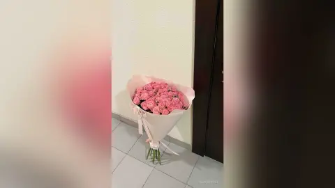 Large bouquet of fresh pink roses wrapped in light pink paper sitting on a tiled floor indoors.