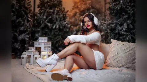 Beautiful woman in white fuzzy winter outfit sitting on a cozy rug in a snowy forest setting.