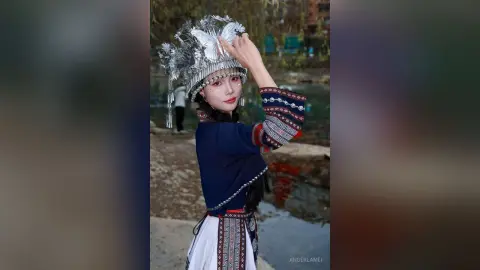 Young woman in traditional silver ethnic costume and ornate headpiece posing outdoors in a serene garden setting.