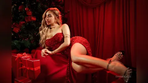 Glamorous woman in a sparkling red sequin gown posing by a Christmas tree and gifts in a festive red setting.