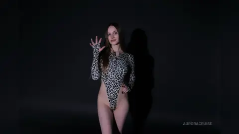 Young woman in a leopard print bodysuit posing against a dark studio background with dramatic lighting.
