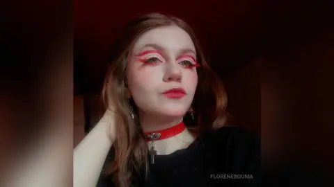 Young woman with dramatic red winged eyeliner and a black outfit posing in moody red lighting.