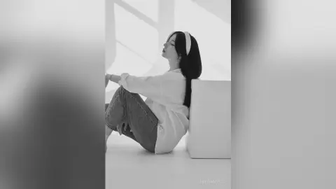 Dreamy black and white portrait of a woman in a white shirt sitting peacefully in a bright, minimalist room.