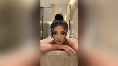 Young woman with wet hair bun leaning on a marble counter in a luxury bathroom setting.