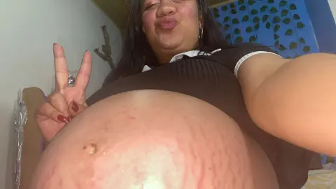 Close-up of a pregnant woman in a black top showing her baby bump in a bright indoor setting.