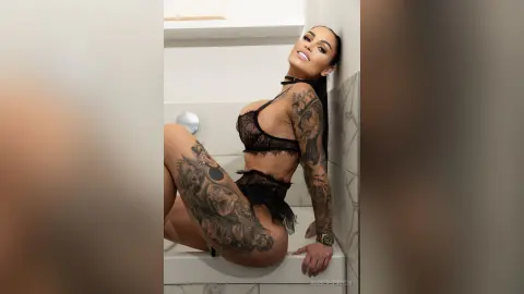 Smiling tattooed woman in black lace lingerie posing in a bright modern bathroom.
