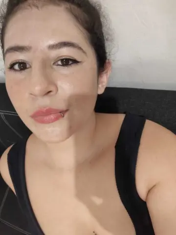 Close-up portrait of a young woman with winged eyeliner wearing a black tank top in a bright indoor setting.