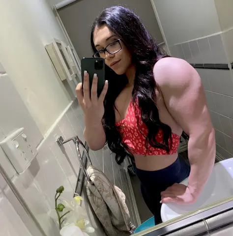 Muscular woman in a red leopard print crop top taking a confident mirror selfie in a modern bathroom.