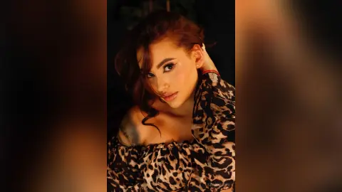 Glamorous woman in a leopard print blouse posing with a moody, warm studio lighting aesthetic.