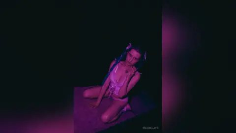 Young woman in pink lingerie sitting on a floor in moody, purple neon lighting.