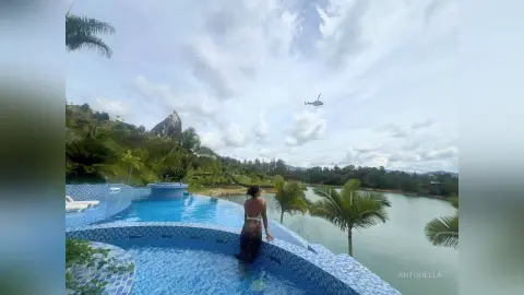 Woman in a white swimsuit relaxing by a luxury infinity pool overlooking a tropical lake and mountains.