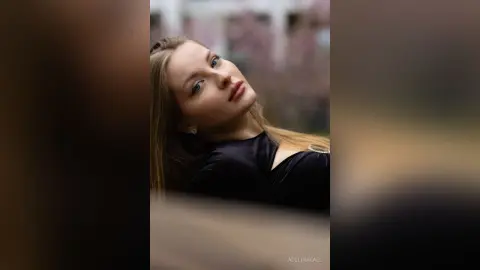 Portrait of a blonde woman in a black top posing with a serene expression in a soft-focus outdoor setting.