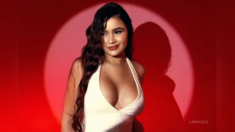 LaraCole poses in a white low-cut top with her long wavy hair down against a red background.