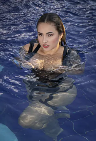 PaolaReyy — PaolaReyy wades in deep blue water wearing a black mesh bodysuit, her wet hair slicked back.