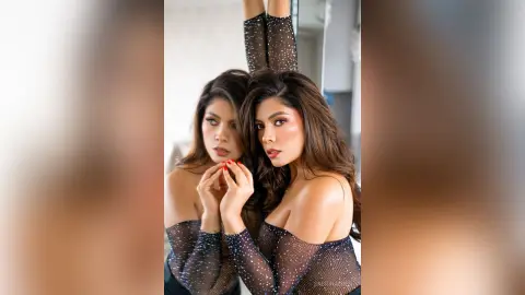 Glamorous woman in a black sheer sparkly top posing for a portrait in a bright indoor setting.