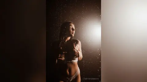 Moody portrait of a woman in white lace lingerie under dramatic golden lighting and falling water droplets.