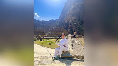 Woman in white outfit sitting on stone steps at an ancient mountain ruins site under a bright blue sky.