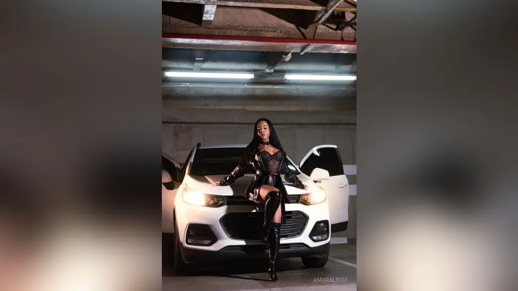 AmaraLisse — AmaraLisse sits on the hood of a white car wearing a black lace bodysuit and thigh-high boots.