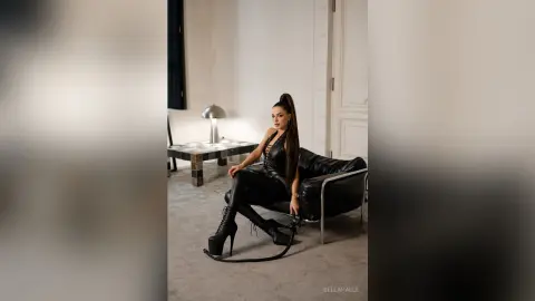 Stylish woman in a black leather outfit sitting on a sofa in a modern minimalist living room.