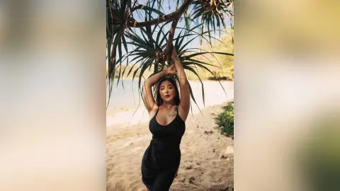 Woman in a black dress standing under tropical palm trees on a sunny beach.