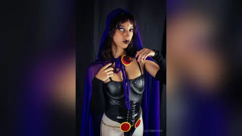LilithBrooks wears a black leather corset and a blue hooded cape, posing against a dark background.