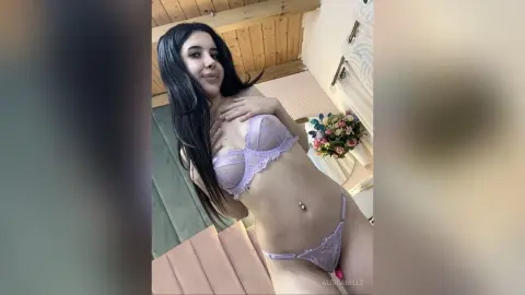 Young woman with long dark hair wearing lavender lace lingerie in a bright indoor setting.