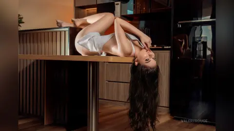 ValeryRouge arches her back while lying naked on a wooden table, letting her long dark hair hang down toward the floor.