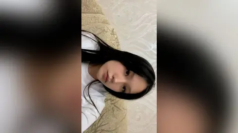 Young woman with long dark hair wearing a white t-shirt relaxing in a cozy indoor setting.