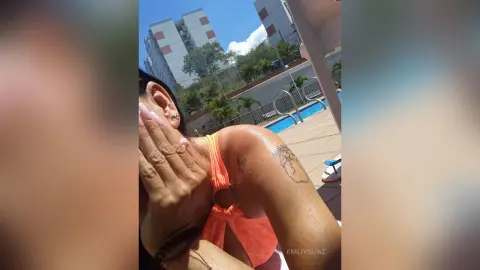 Woman in an orange bikini relaxing by a sunny outdoor swimming pool on a bright summer day.