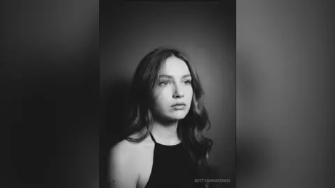 Moody black and white portrait of a young woman in a black halter top against a dark studio background.