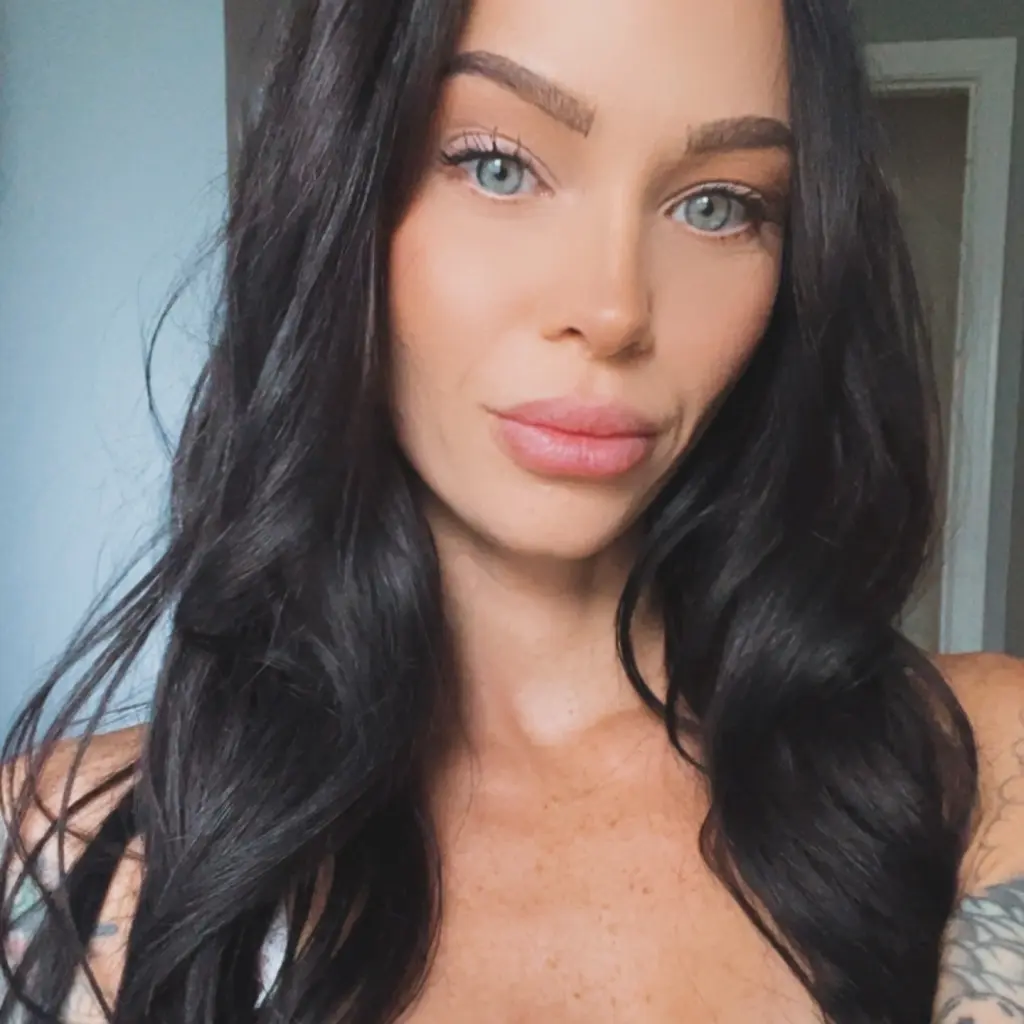 Stacy_babyy poses with a pink lollipop, wearing a black tank top and a black choker, with her black hair styled in two buns.