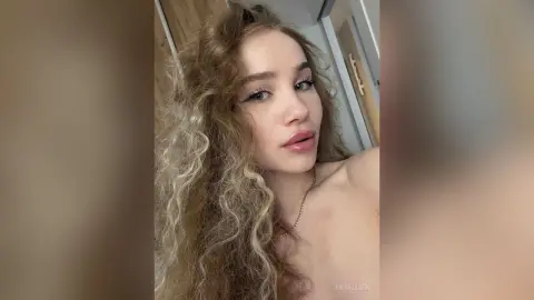 Young woman with long curly blonde hair posing in a bright indoor setting with a soft, natural mood.