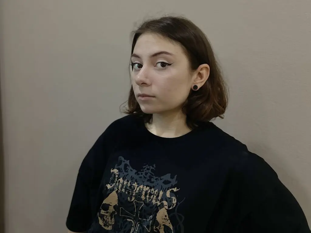 Young woman with winged eyeliner wearing a black graphic t-shirt in a minimalist indoor setting.