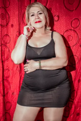 Confident woman in a black mini dress posing against a red patterned backdrop.