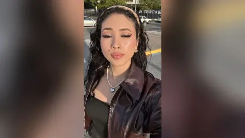 Young woman with wavy hair wearing a brown leather jacket and pearl necklace outdoors during golden hour.
