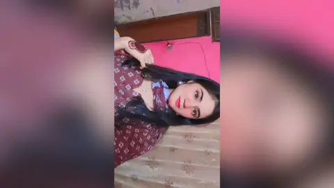 Young woman in a patterned maroon blouse smiling in a cozy indoor setting.