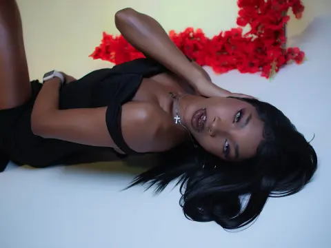 Elegant woman in a black dress lying on a white floor with red floral decor in a moody studio setting.