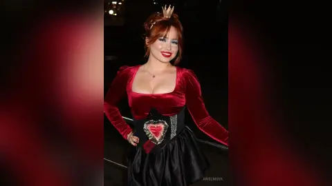 Smiling woman in a red velvet dress and black skirt posing at a glamorous evening event.