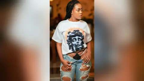 Young Black woman in graphic white t-shirt and ripped jeans posing with a confident expression indoors.