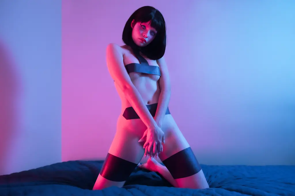 Woman with futuristic blue eye makeup and glitter in a neon-lit cyberpunk setting.