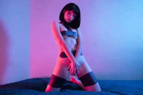 Moody portrait of a woman in black lingerie posing on a bed under pink and blue neon lighting.